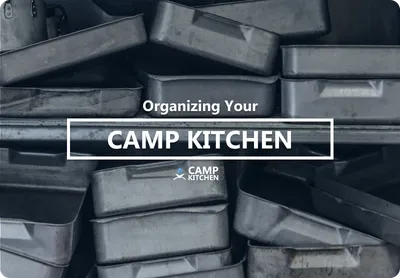 Stacked stainless steel gastronorm pans on a shelf in a commercial camp kitchen.