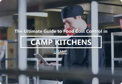 A camp kitchen manager reviewing food cost figures on a tablet beside a stainless steel prep counter.
