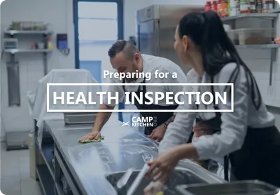 Two kitchen staff sanitising a stainless steel prep surface ahead of a health inspection.